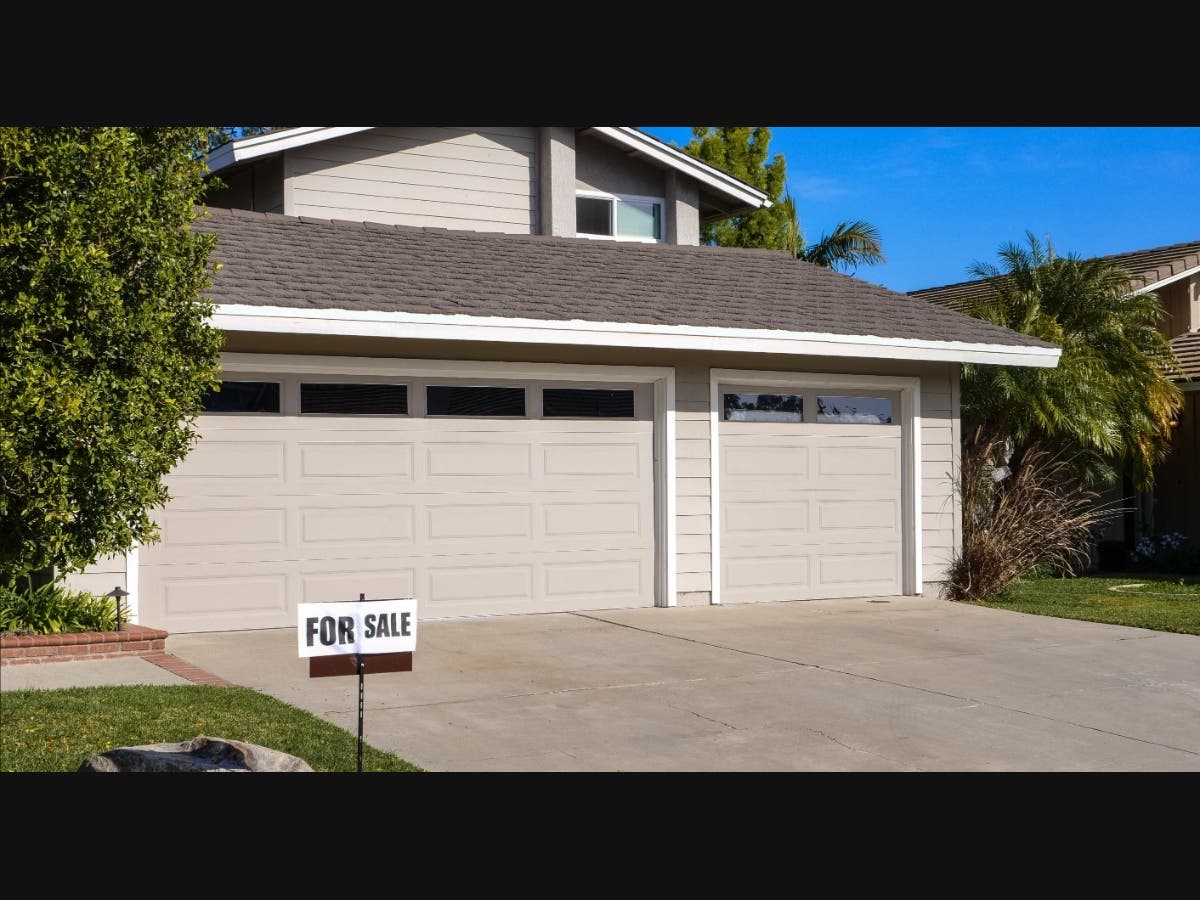 Modern residential house with a two-car garage and a for sale sign.