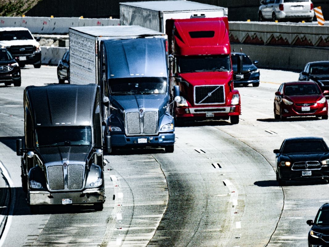 Three large trucks taking a turn on the freeway in three of the lanes.