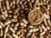 A jar of peanut butter surrounded by peanuts.