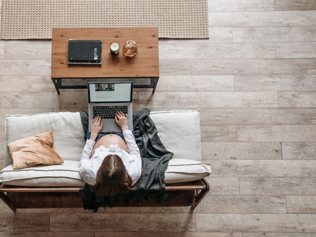 Expectant mother working from home on a laptop, sitting comfortably on the floor near a couch.