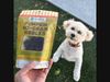 A small white dog eagerly looks up at a bag of TerraPawz Pumpkin No-Grain Nibbles.