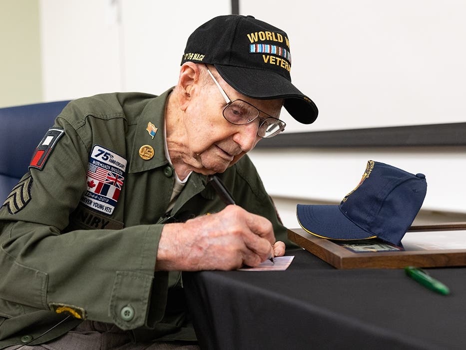 Andrew 'Tim' Kiniry, of Minotola, signs a baseball card of himself after the 104-year-old World War II veteran spoke to a group of students and community members at Stockton University on April 16.