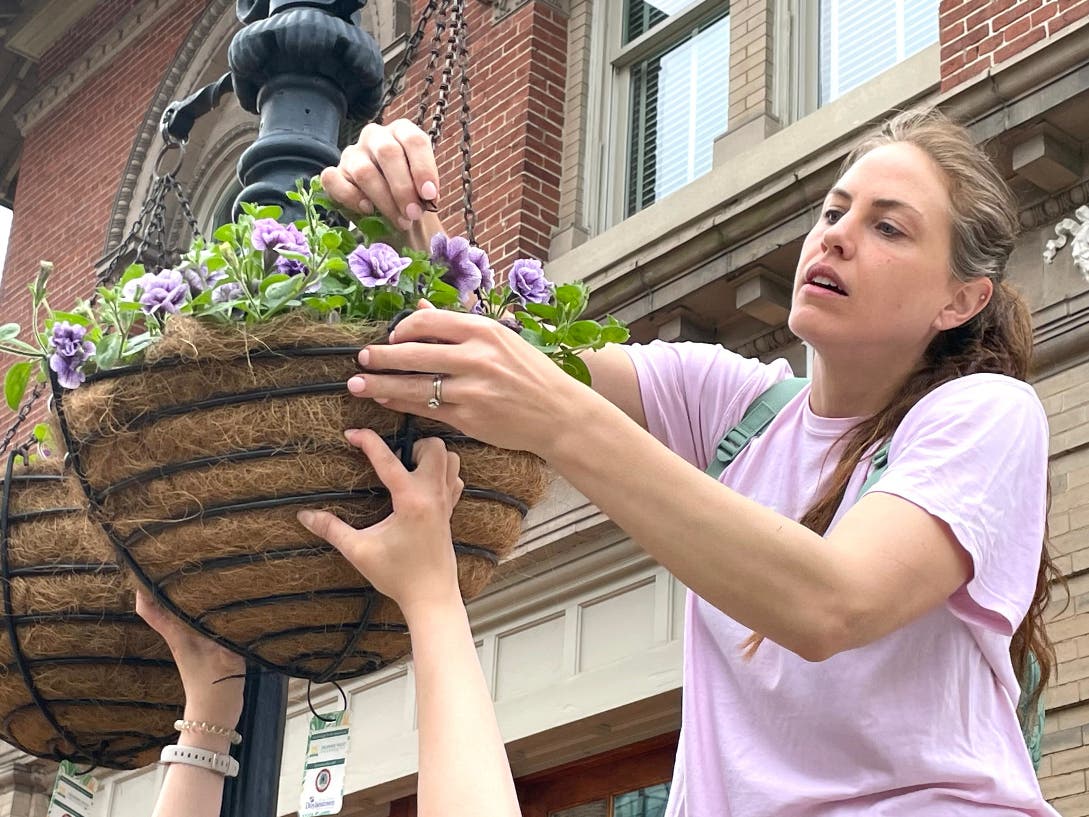 Becca Rosen, assisted by Brianna Meisenbacher, hangs a basket in front of the fire station on Shewell Avenue.