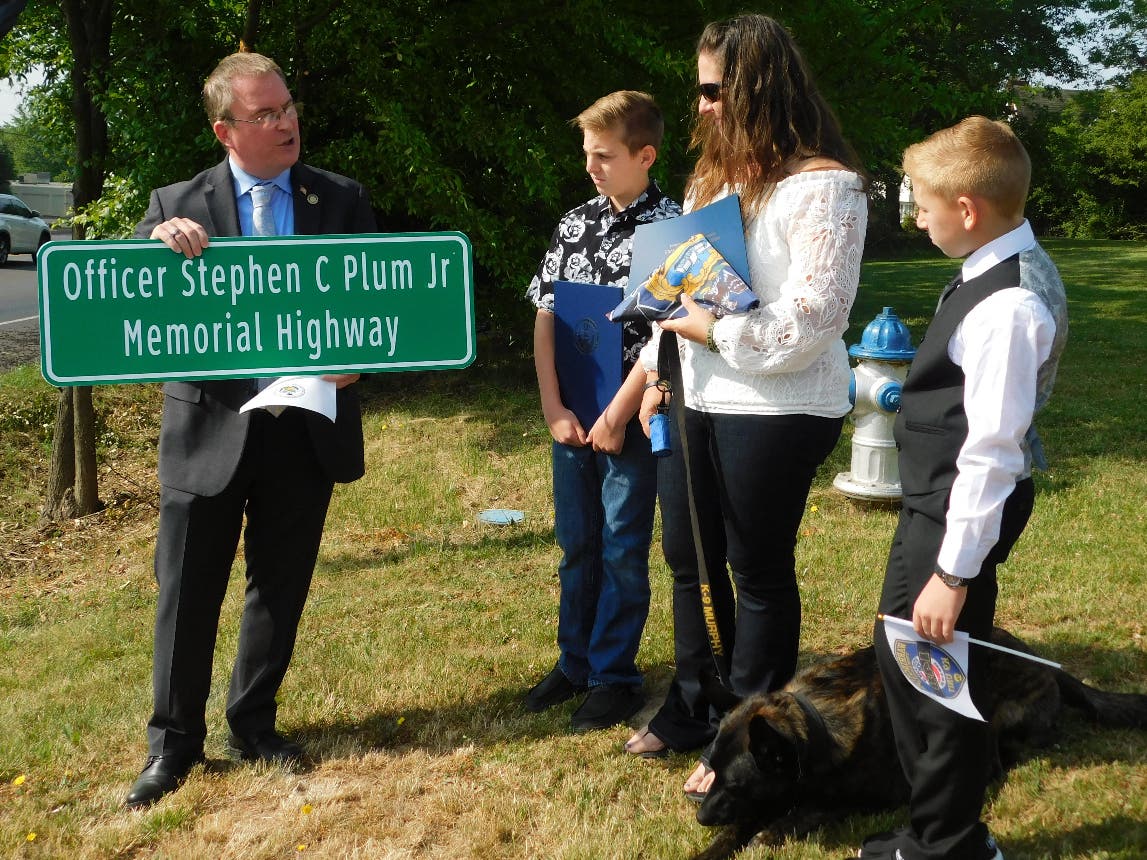 State Rep. Brian Munroe presents a commemorative copy of the sign to Officer Plum's family during the ceremony.