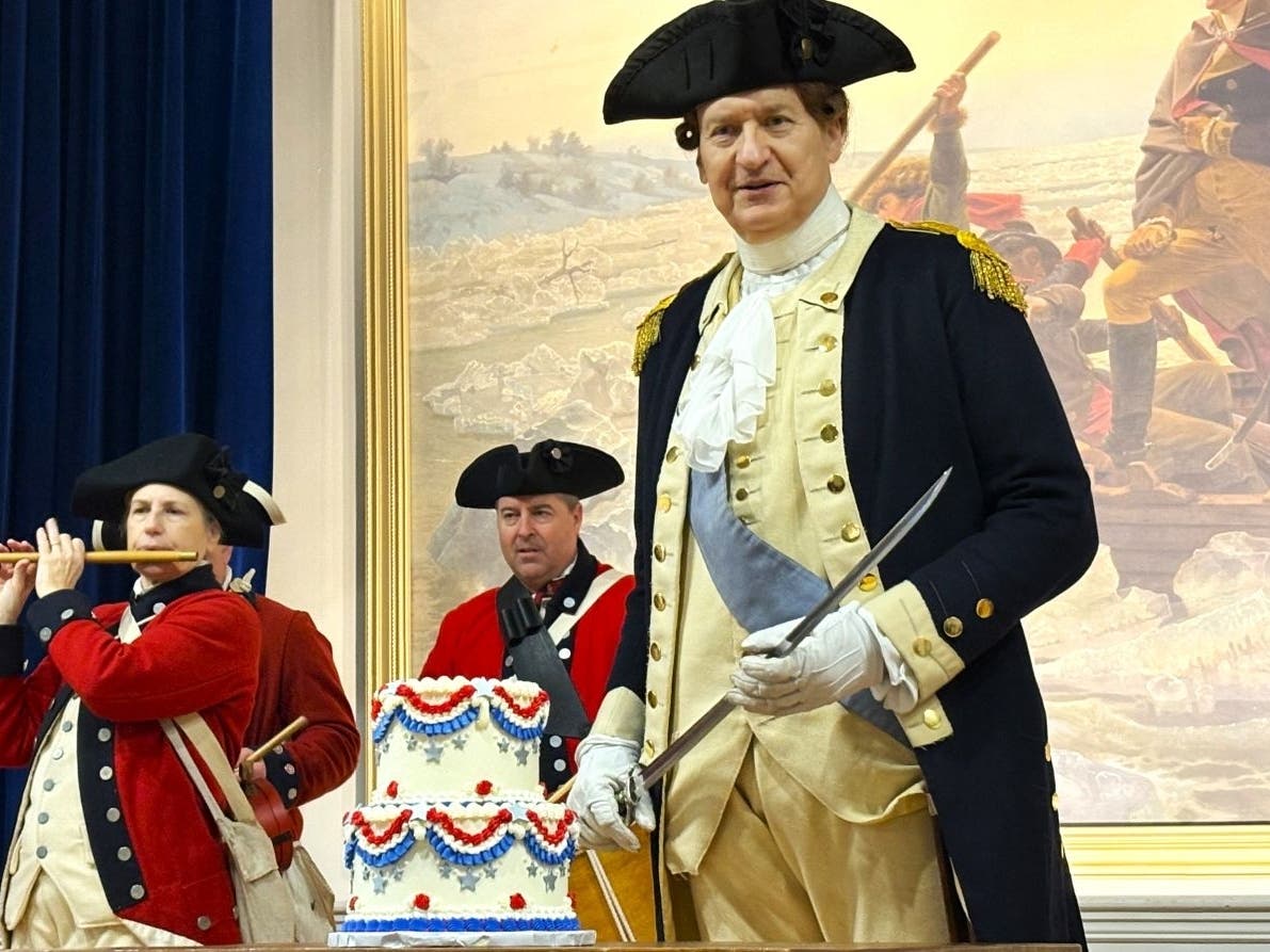 George Washington portrayed by John Godzieba prepares to cut his birthday cake with the sword.