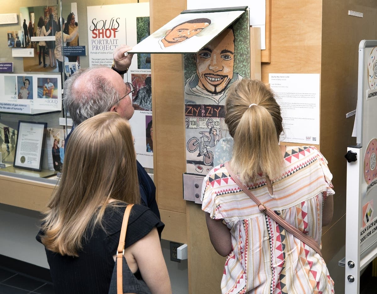 Visitors to the Gallery at Lower Bucks Campus examine an interactive display that tells
the story of a young man lost to gun violence as part of the “Souls Shot Portrait Project”
on display through September 17.