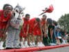 A member of the Jesse White Tumblers flies over Illinois School students, fellow team members and the Illinois school mascot.