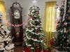 A traditional green Christmas tree filled with red and white decorations stands elegantly between a classic grandfather clock and modern festive touches.