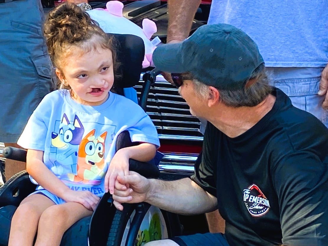 The JP Emerson Show host JP Emerson shares a smile with a young resident at a past "Horsepower and Hope" event, bringing classic car culture and community support directly to pediatric medical families navigating crises. 