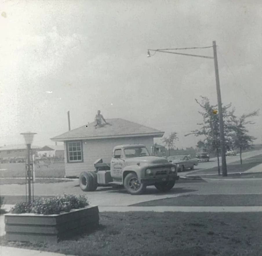 black and white photograph of the first official library building on 171st st in 1956. A truck is delivering the portable building, and a man is sitting on the roof.