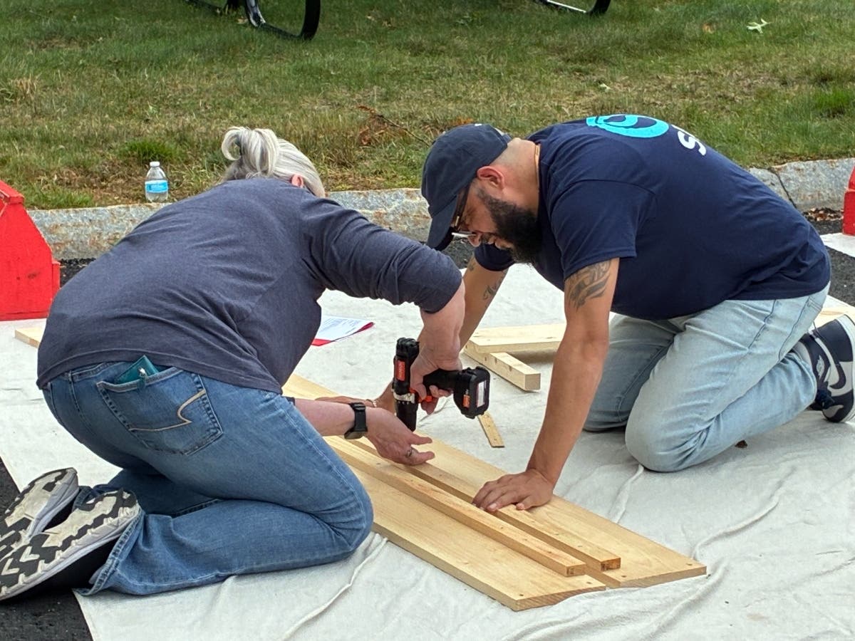 St. Mary’s Credit Union employees assemble wooden bed components outside the institution’s Marlborough headquarters on Sept. 30. The employees built 10 beds for children in partnership with A Bed for Every Child.