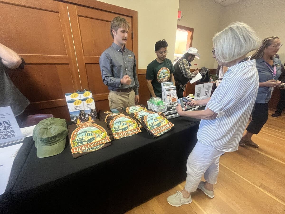 A woman considers SMART swag at an Aug. 10, 2026 community town hall in Geyserville hosted by the agency. The vote announced Aug.19, 2026 moves the Geyserville station into regional planning, development, and funding, but does not authorize construction.