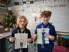 Middle school students smile as they hold illustrated character-trait worksheets in their classroom.
