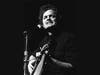 Harry Chapin pauses between lyrics while holding his acoustic guitar, a signature image of the singer-songwriter known for blending music with social action.