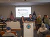 Town of Babylon Sustainability Director Jassi Anand stands alongside a presenter at the podium during opening remarks at Green Horizons 2.0, highlighting local efforts to promote environmentally responsible practices.