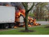 A tractor-trailer burns along the roadside in Hauppauge, with flames consuming the cab as firefighters respond nearby.