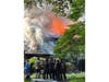 Firefighters and emergency personnel gather outside the Oakside Drive home as flames burn through the roof.