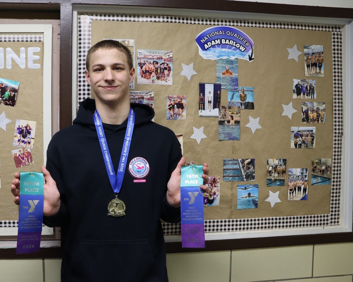 Adam Barlow displays his first place medal and ribbons awarded at YMCA national competition in front of the inspiration board highlighting his swim career outside the aquatics center of the Bethlehem branch of River Crossing YMCA.