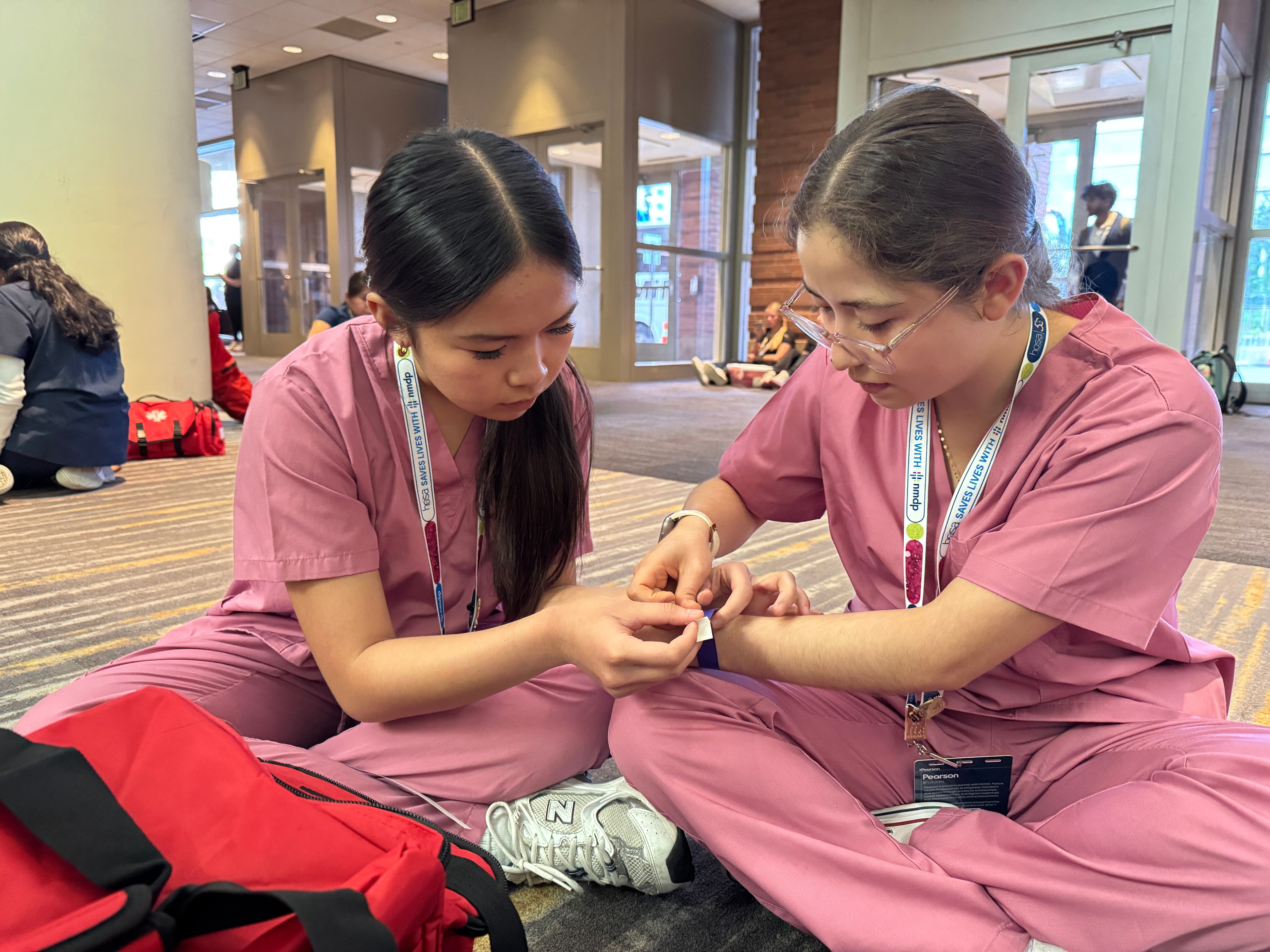 Two Harmony School of Innovation-Fort Worth students in pink scrubs practice a CPR/First Aid skills scenario during the HOSA International Leadership Conference.