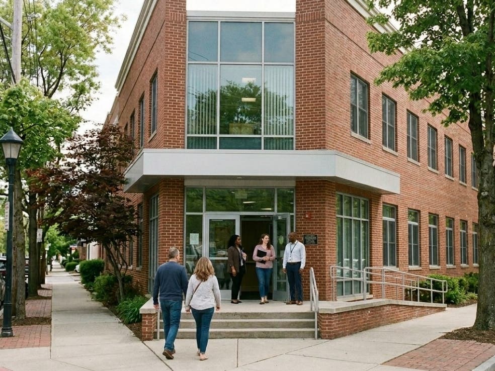 A view of the main entrance to a brick office building on a tree-lined street corner.