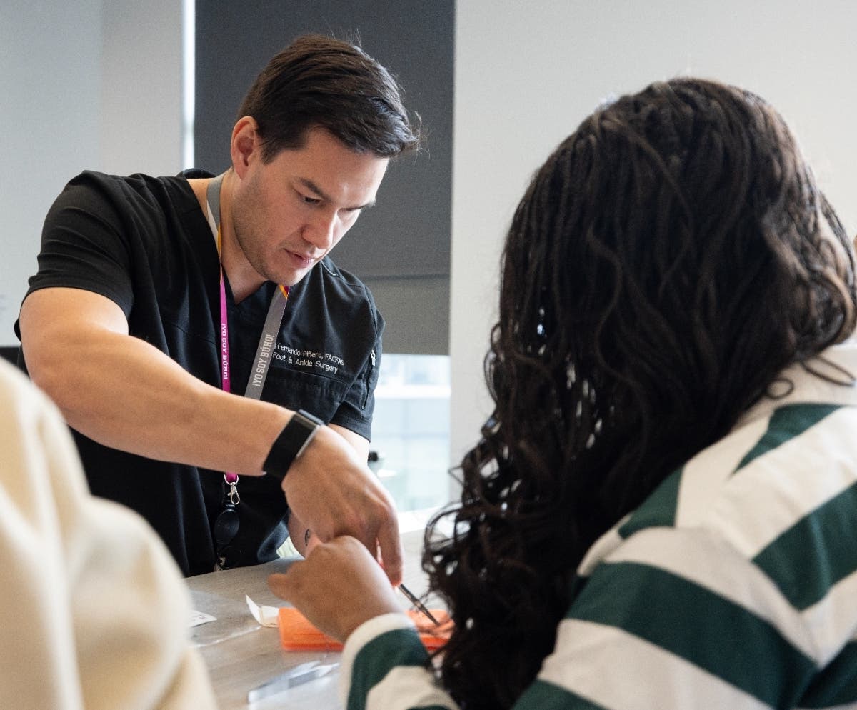 Dr. Fernando Piñero, left, a podiatric foot and ankle surgeon and NYCPM graduate, teaches Quinnipiac students basic suturing techniques during a recent clinic.