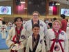 (Front row, left to right) Kataliena holding her 2 Gold and Silver medals, Matteo wearing his championship Silver medal, and Kora showing off her Bronze medal in Sparring, with their instructor Master Virginia Folger standing proudly behind them!