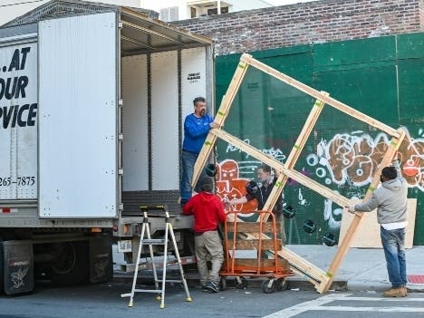 Movers placing a large square wooden frame into a moving truck