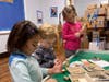 UPMS students tinkering with Makerspace supplies to add to the "city" built during an earlier visit to the Makerspace room, as seen in the background.