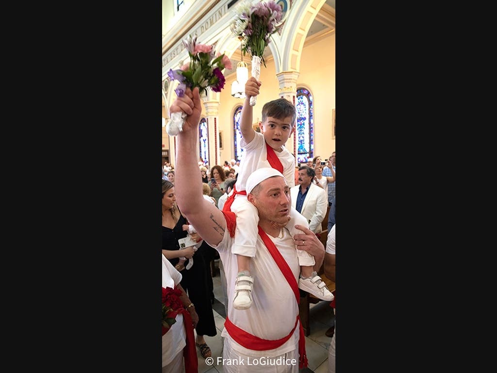 A father-Sebastian Liseo- carries his son on his shoulders inside the St. Sebastian's Church in Middletown and they are saying “E Chiamamulu Paisanu! Primu Diu E Sammastianu!” before the statue is taken out of the church.