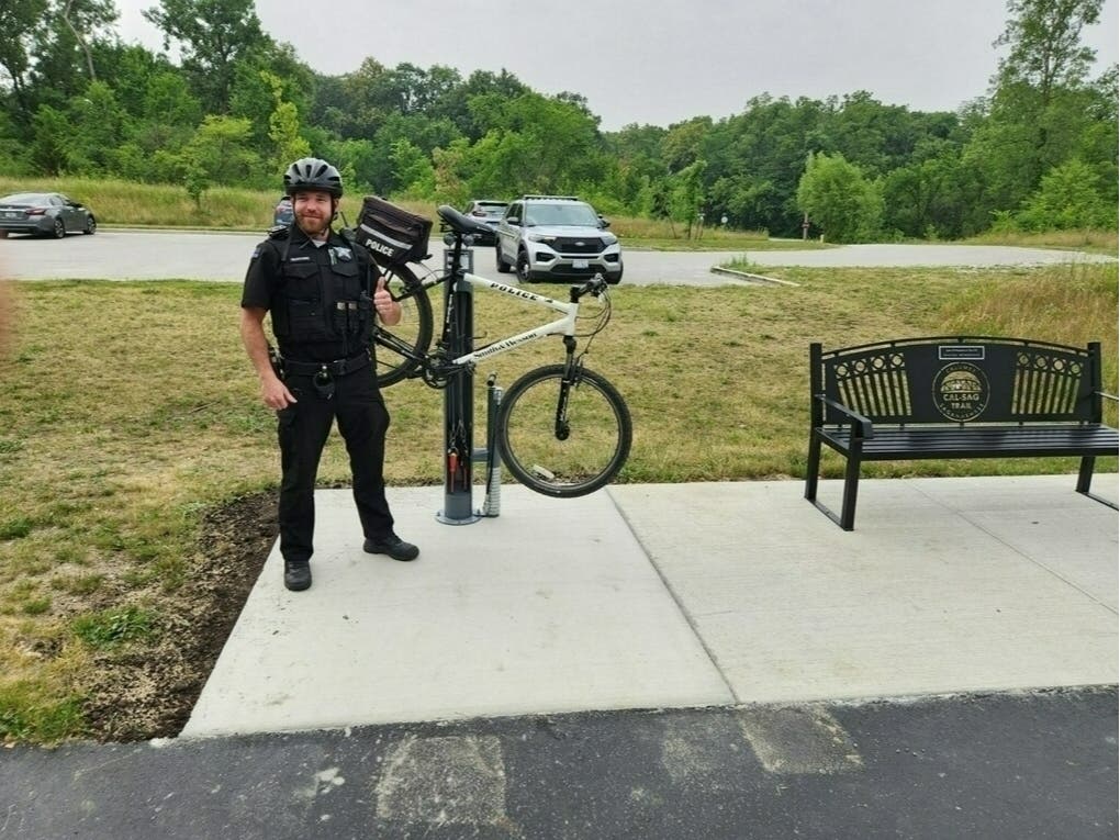 New Officer Cohen Piechocinski, of the Palos Park Police Department, gives a thumbs up to the new bike fix-it station at the Cal-Sag Trailhead. 
