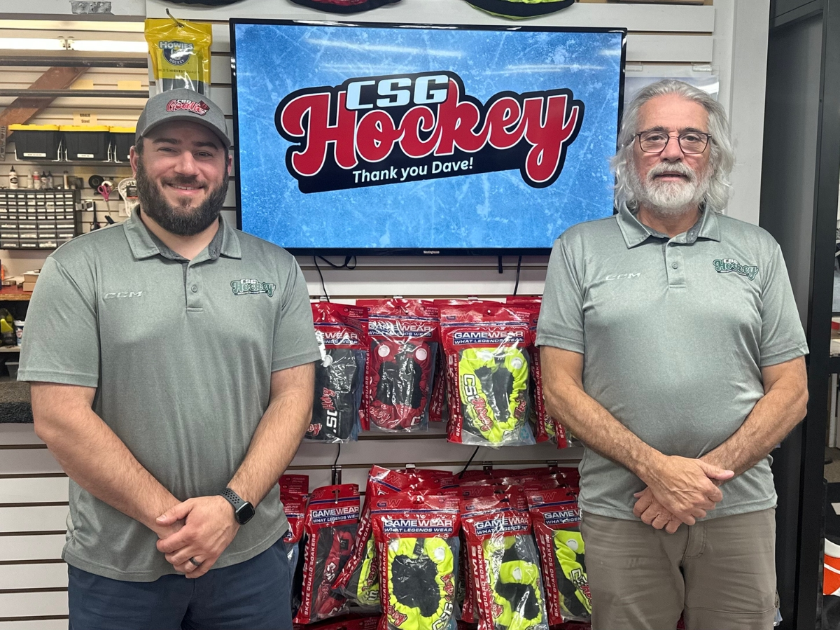New CSG Hockey owner Zac Guercia poses with long-time store owner Dave Palisi in the Concord store. In the background, a digital display shows the CSG Hockey logo with a message that says