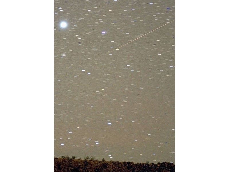 The Geminid meteor streaks diagonally across the sky against a field of star trails in this 1.5-minute exposure.