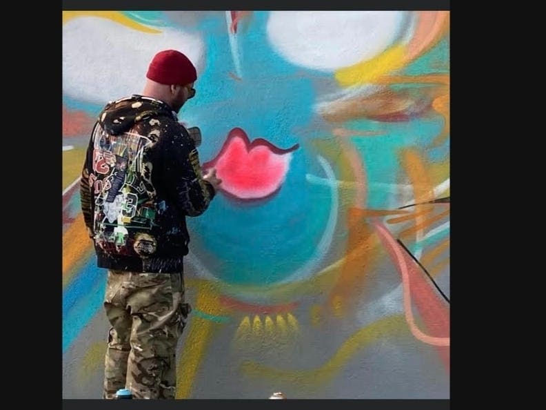 Artist Spencer Stown painting an abstract expressionism mural outside of a Flower Hill business that has now been ordered covered by village officials.