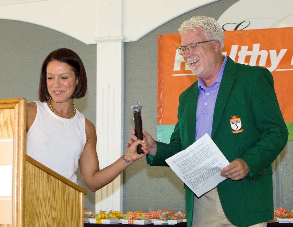 Dionne Miller, ABC7 weekend sports anchor/reporter and celebrity guest for the Edward Foundation Charity Golf Tournament, hands off the microphone to Joe Dant, President & CEO, Edward Hospital, at the event’s award ceremony on July 19.