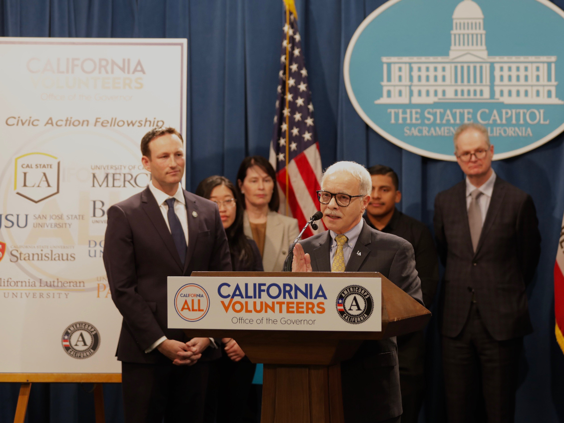 Cal State LA President William A. Covino speaks at a lectern during the news conference alongside California's Chief Service Officer Josh Fryday and officials from the other universities participating in the new fellowship program.