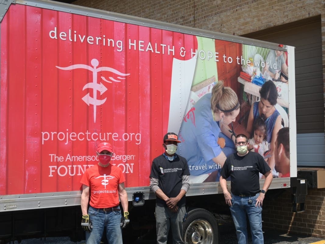 Project C.U.R.E. volunteer driver Larry Colletta, UMMS warehouse employee Ed Belcher and Jason Fraker, manager of the University of Maryland Medical System warehouse, gather outside the Project C.U.R.E. truck.
