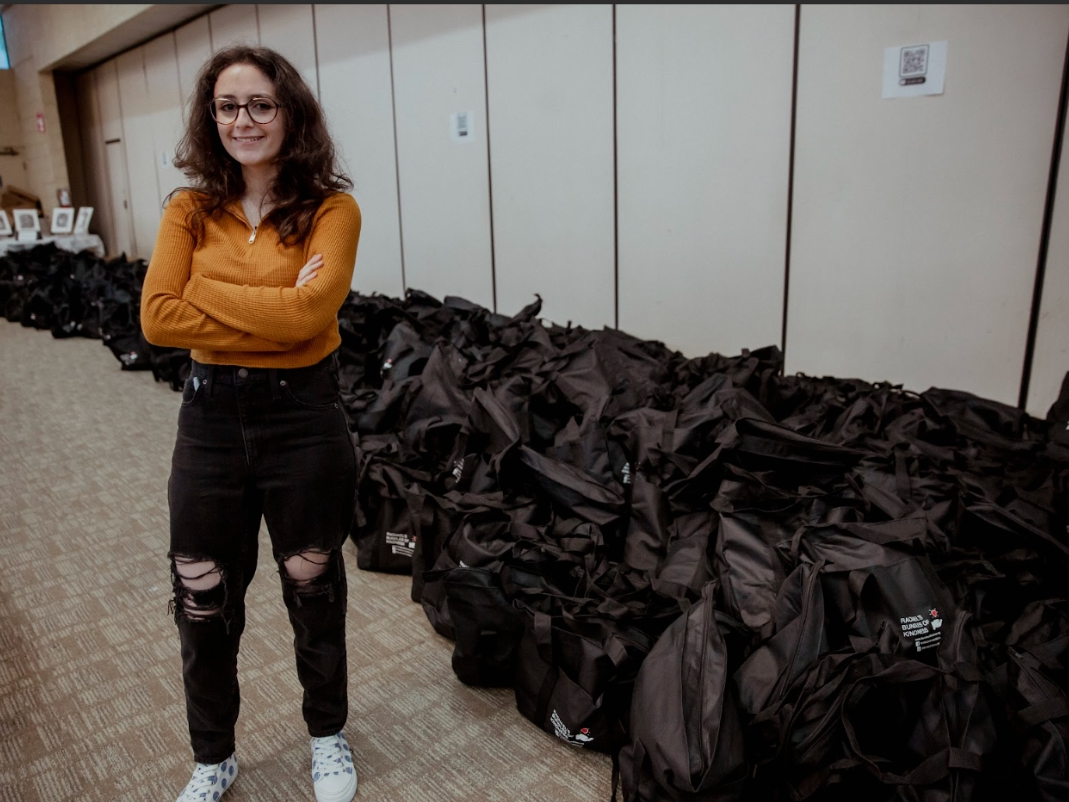 Rachael Rosenberg stands next to hundreds of bundles filled with necessities to help people living on the street.