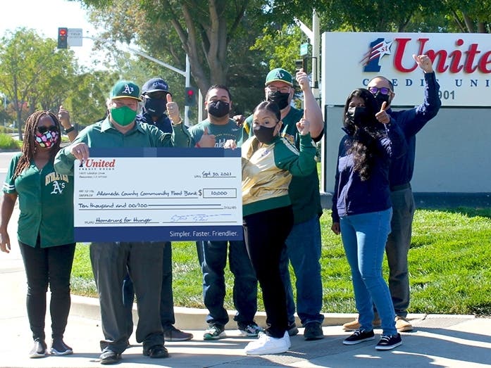 1st United Credit Union staff showing their A's pride while holding a check for the Food Bank