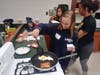 Christiane Gbabiri (Stagg), Demi Wojdula (Stagg), and Arienne Monteclar (Sandburg), chatting  in French while cooking.