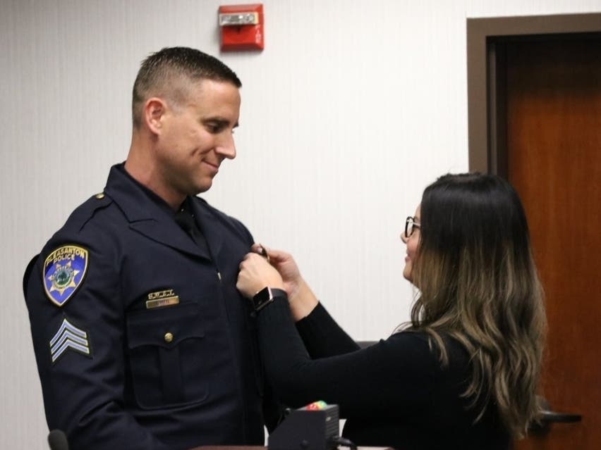 Officer Anthony Pittl ​gets his new badge pinned on by his wife.